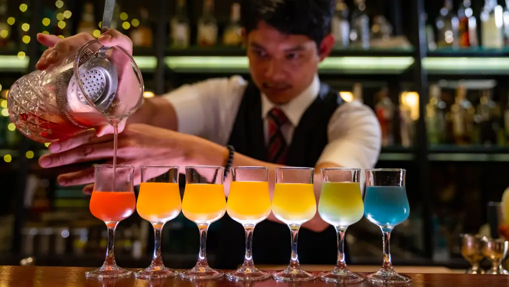 image of Professional male bartender preparing colorful cocktail drink serving to customer on bar counter at nightclub. Barman making mixed alcoholic drink for celebrating holiday event party at luxury restaurant bar.