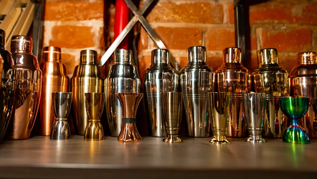 image of easy to story Professional bartender equipment as different metal color jiggers and shakers on the shelf in the bar