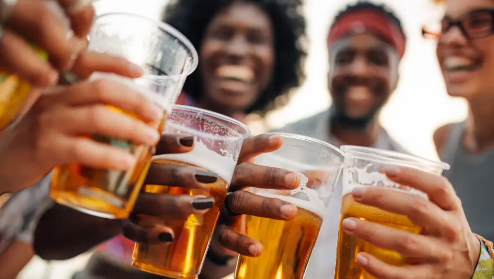 image of Cheerful friends are enjoying a music festival, raising plastic cups of beer in a joyful toast, celebrating friendship and the vibrant atmosphere