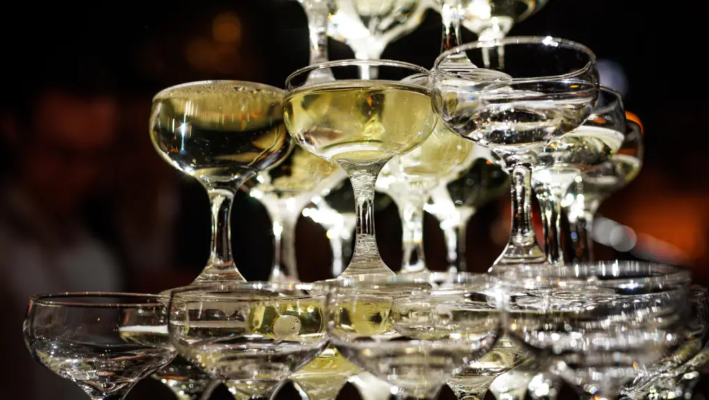 Champagne glasses stacked in a pyramid set against a dark background.