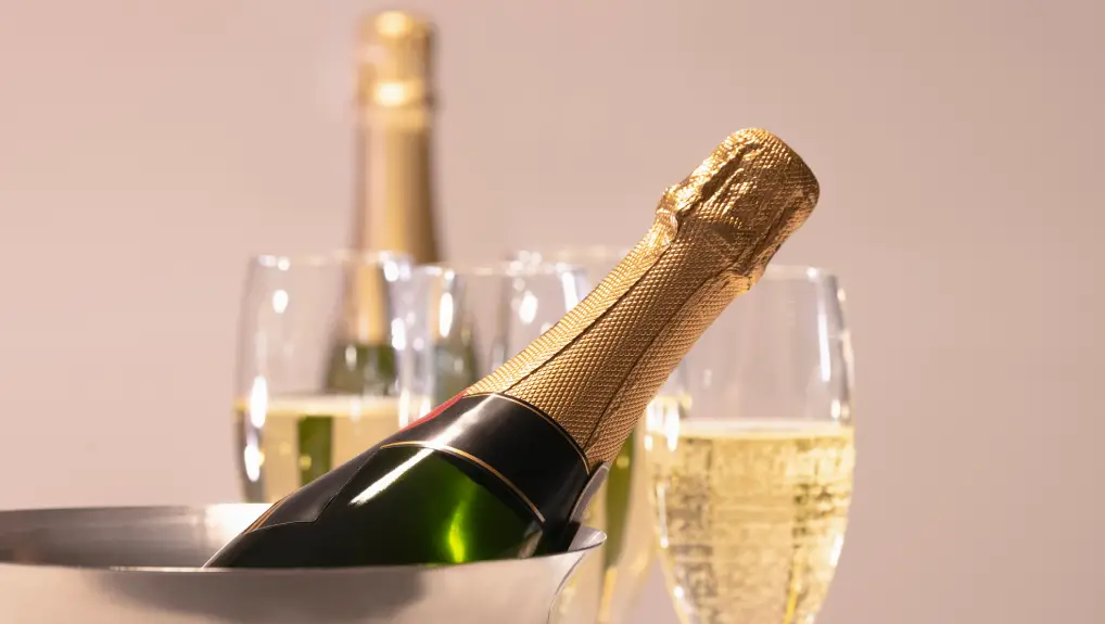 image of Select focus of a champagne bottle inside a champagne bucket with out of focus champagne glasses and bottle at the back. Celebration concept.