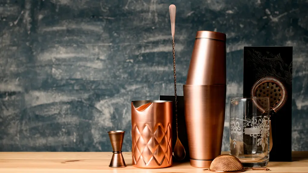 Close-up view on composition with some copper items of bar equipment which stands on wood surface at bar.