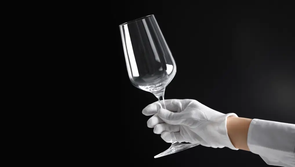 Person in white glove checking cleanliness of glass on dark background, closeup