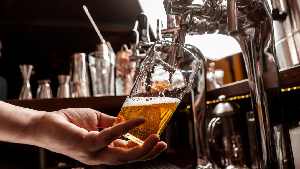 image of Bartenders hand holds glass and takes drink from tap in interior of pub