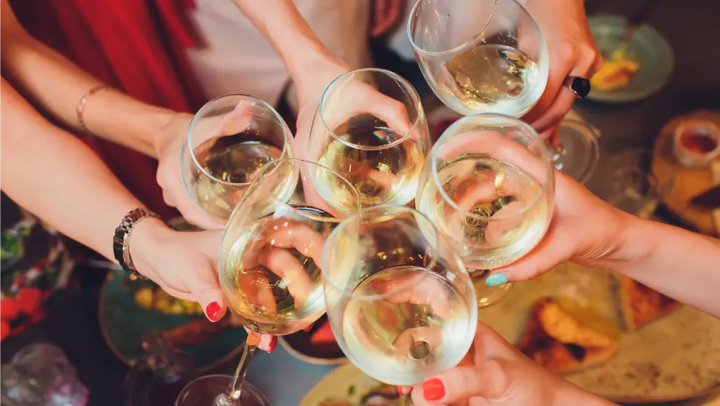 hands with glasses of wine clinking them over served table