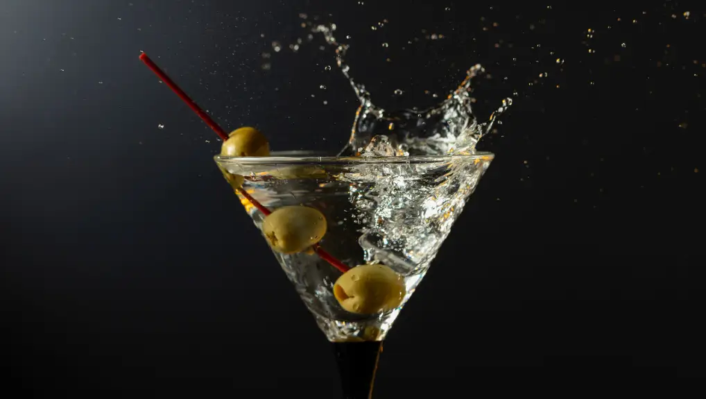 image of Glass of classic dry martini cocktail with green olives on a black background. Martini with splashes.