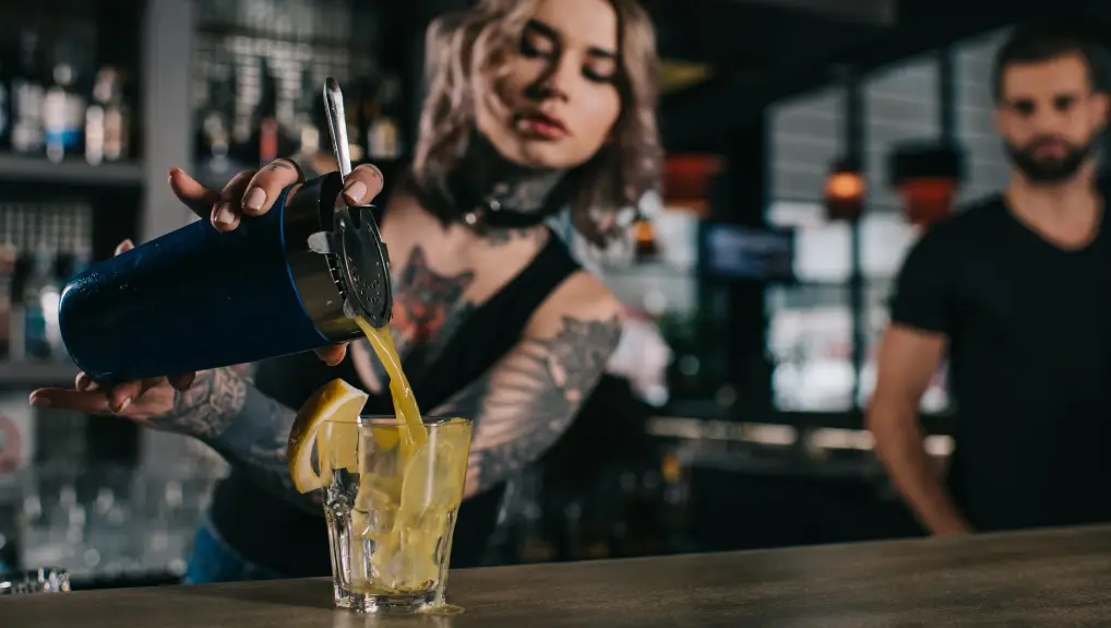 image of tattooed bartender preparing drink at bar with essential bar tools