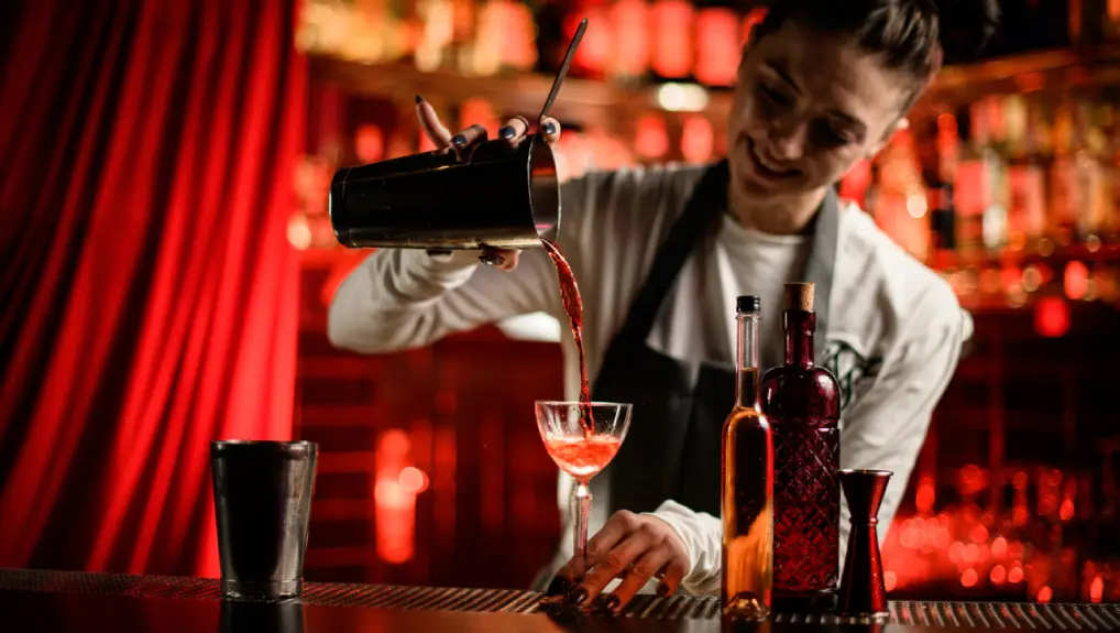 Image of a contemporary bar setting with a bartender pouring a drink from a cocktail shaker.