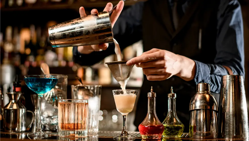 image of a bartender using essential bar equipment. bartender gently pours finished cocktail from the shaker into the glass
