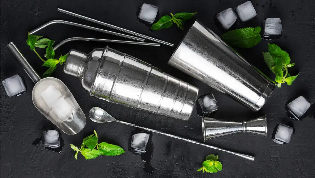 Accessories for making cocktails ,shaker, scoop, straws,jigger,spoon bar ,ice cubes , mint leaves on a dark concrete background