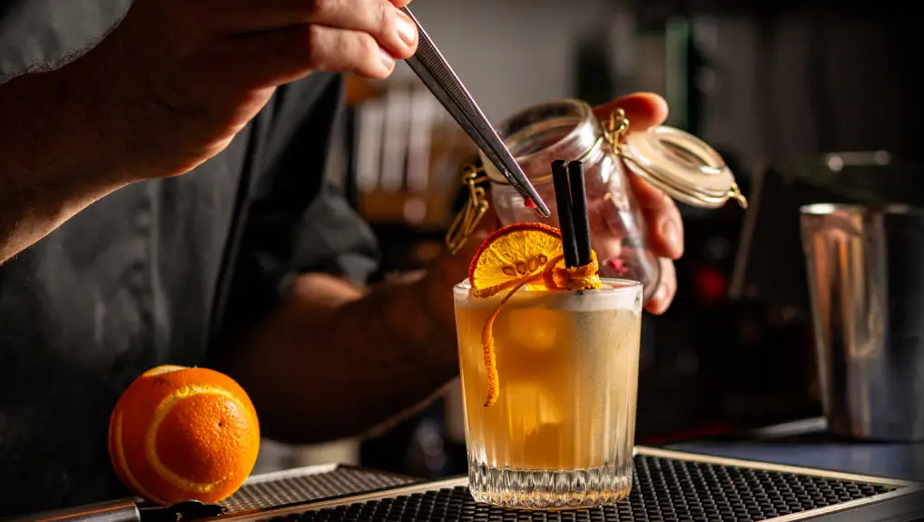 Image of cocktail decorated with Dehydrated Orange Slices and fresh orange peel. Bar or pub interior.
