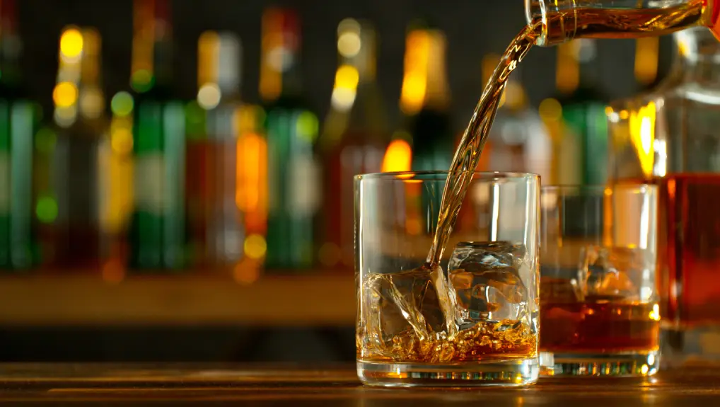 An image close-up of pouring whiskey or rum on the bar, dark toned background