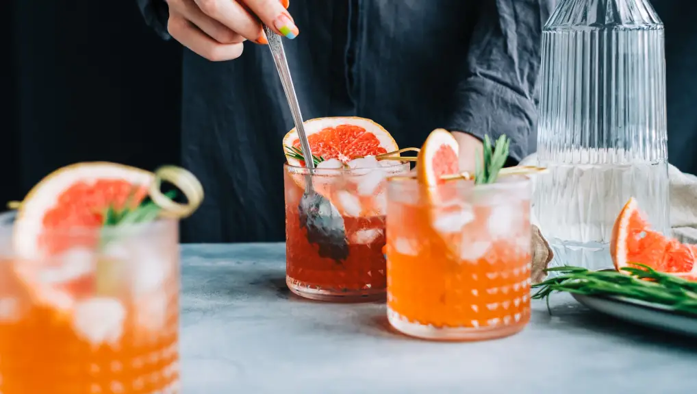 Image of Female bartender cooking fresh lemonade with spoon in glass with ice, grapefruit and rosemary.