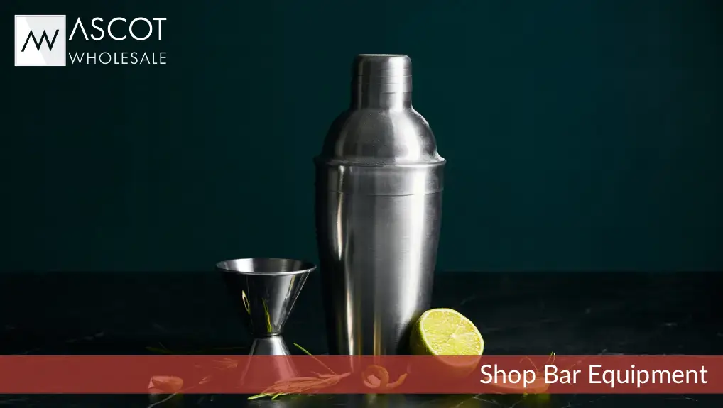 Close-up image of cocktail tools for a beginner, silver cocktail shaker, a jigger and a lime. the image has a dark green background.