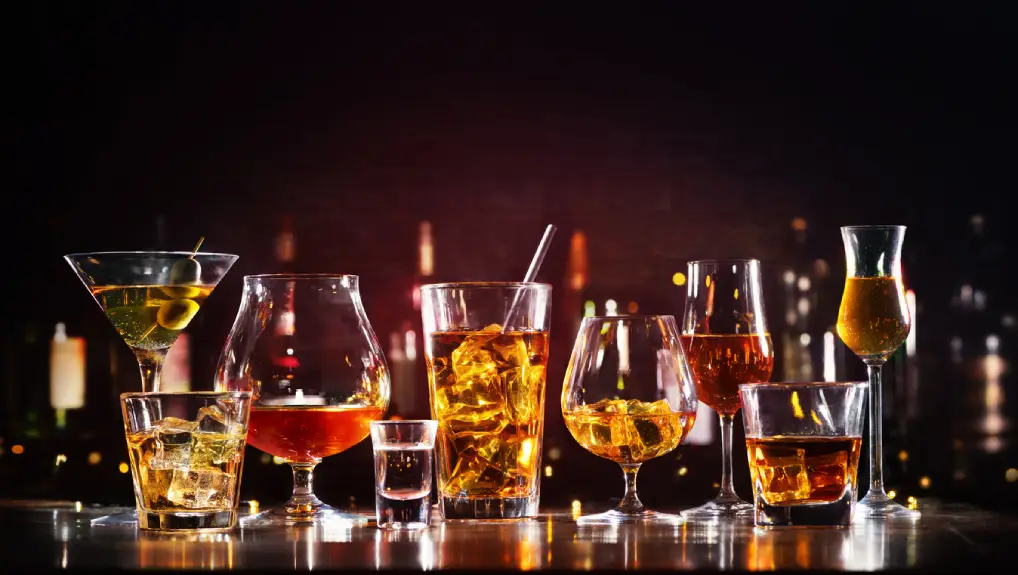 close up image of essential glassware lined up on a bar with various drinks.