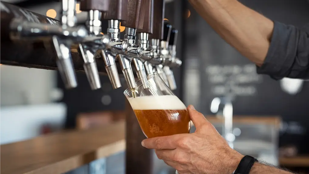Hand of bartender pouring a large lager beer in tap.