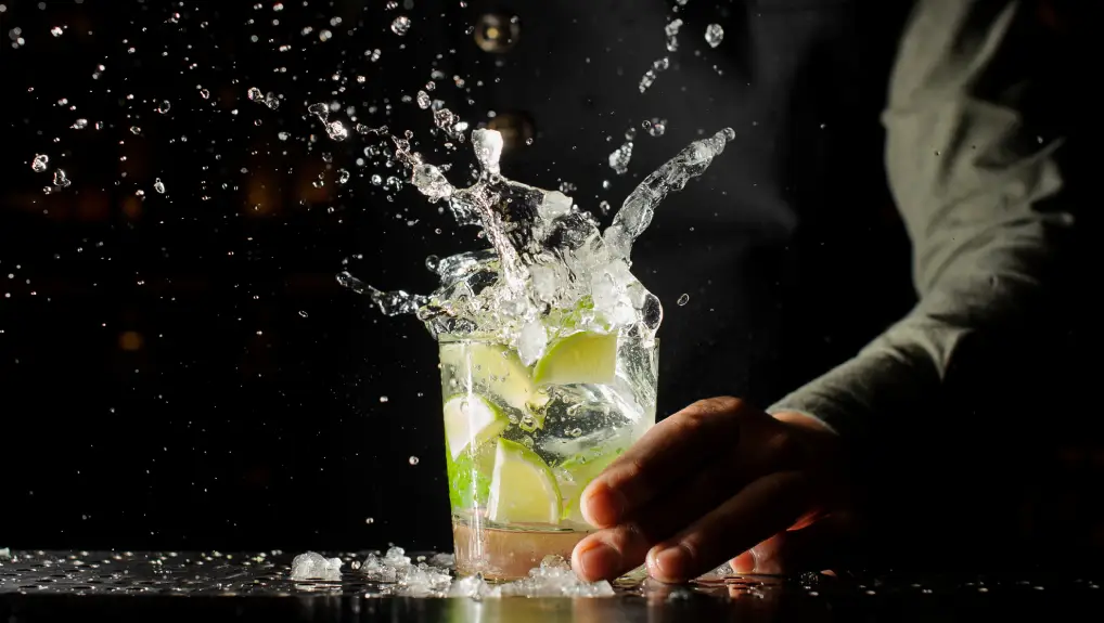 Image of Cocktail splash with ice cubes and lime. Preparing of the delicious fresh cocktail on the bar stand