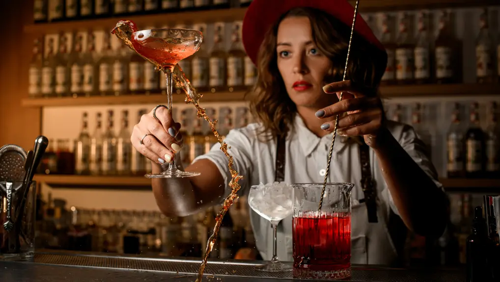 Image of Concentrated bartending woman shakes a cocktail in a mixing glass with one hand and with the other hand shakes the cocktail- showing the impact of mixology tools
