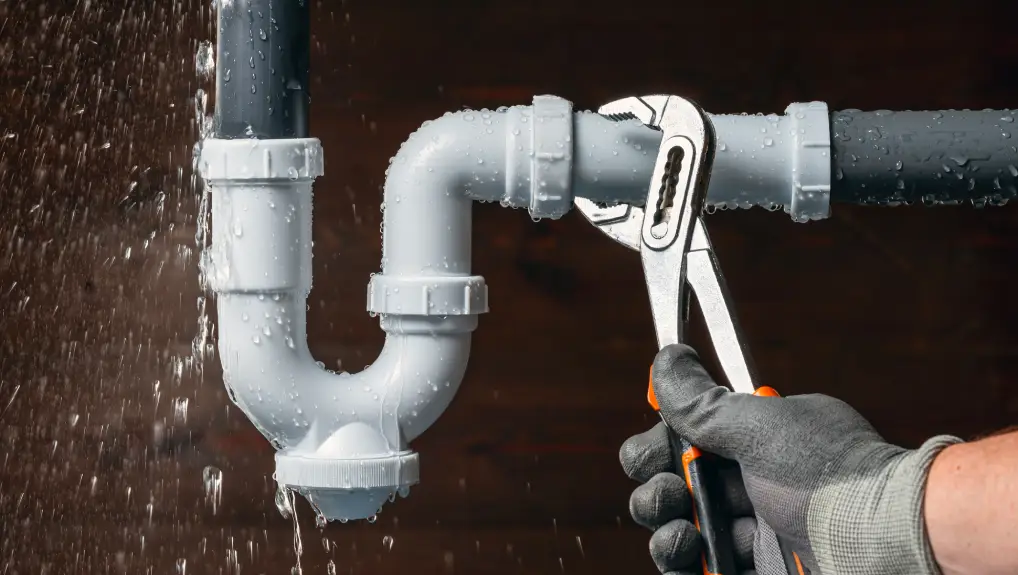 Image of lumber hand fixing a water leak in a sink drain siphon pipe with an adjustable pliers