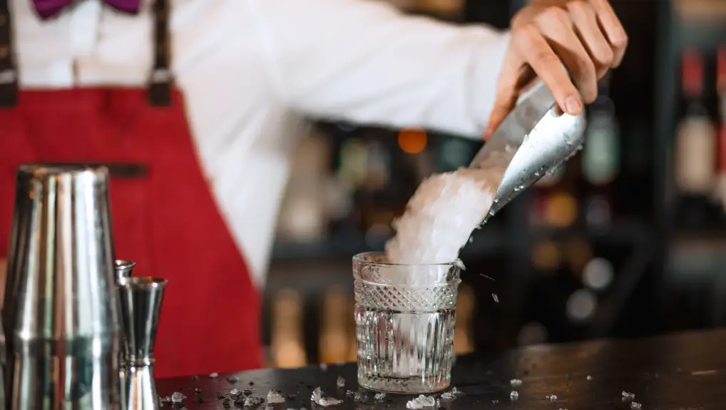 Image of Bartender hand adding ice chips in empty cocktail glass, close up