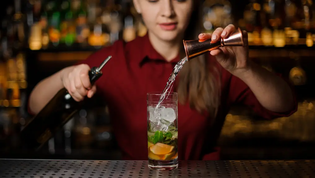 barmaid completes the preparation of the mojito in a crystal glass, adding a white rum, against the bar counter in the bar