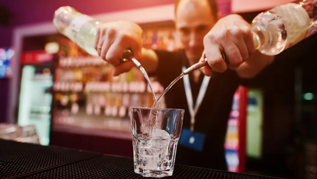 Barman hold bottle with pourer and pouring cocktail at the bar