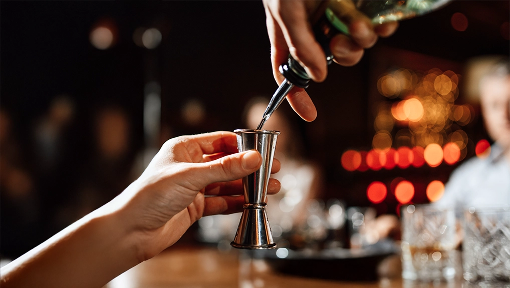 Bartender is pouring drink into the steel jigger. Close-up
