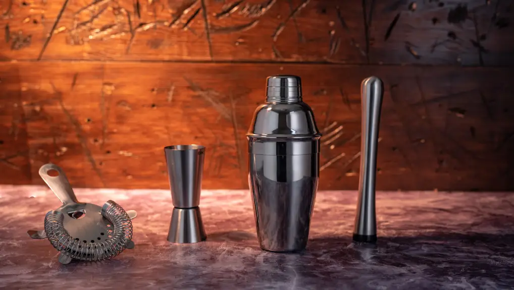 Close up studio image of a cobbler cocktail shaker along with other bar tools