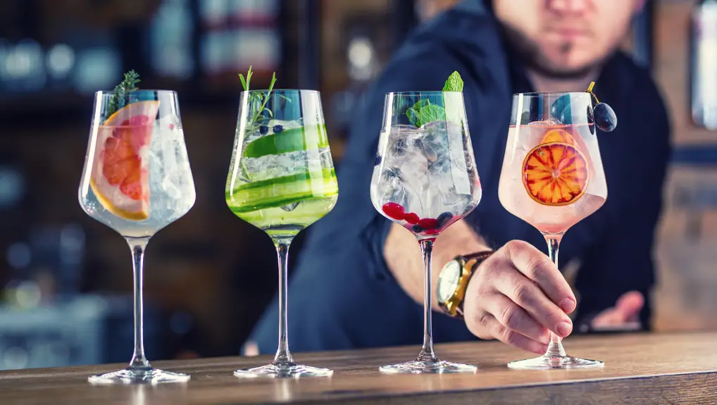 Barman in pub or restaurant preparing a gin tonic cocktail drinks in wine glasses.