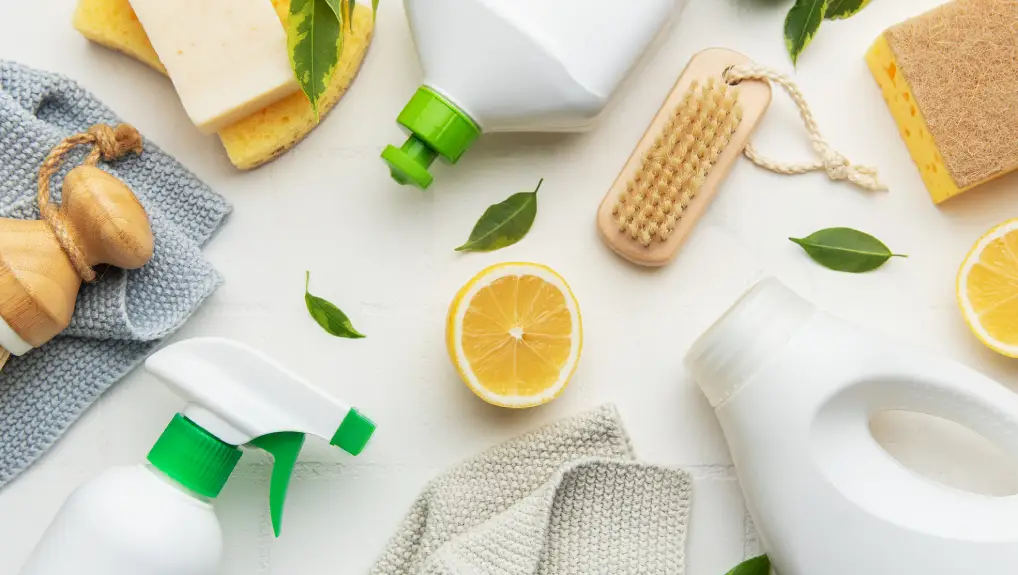 Image of cleaning products, lemon slices, brushes and sponges arranged on white surface