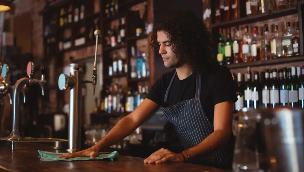 Image of Young waiter cleaning a counter in pub