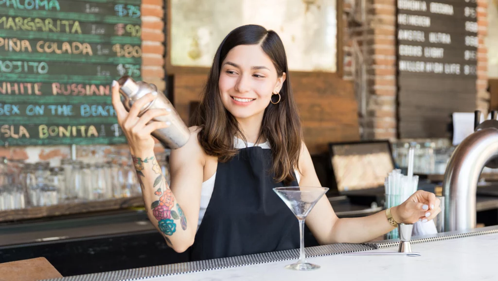 Image of female mixologist practicing and preparing cocktail in shaker at bar counter
