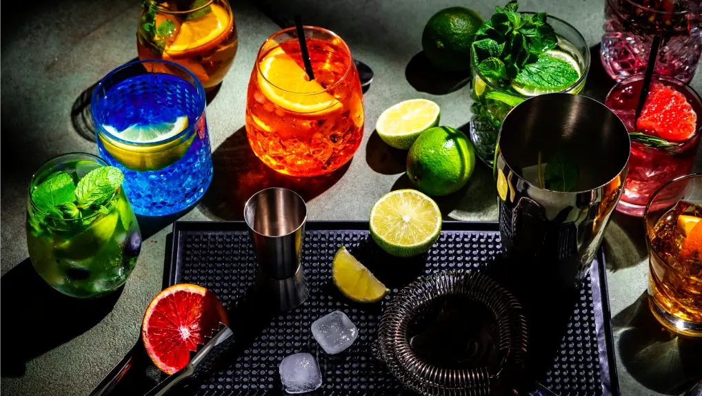 image of bar set up with a selection of cocktails made with garnish and tools scattered- Bar Tool Checklist