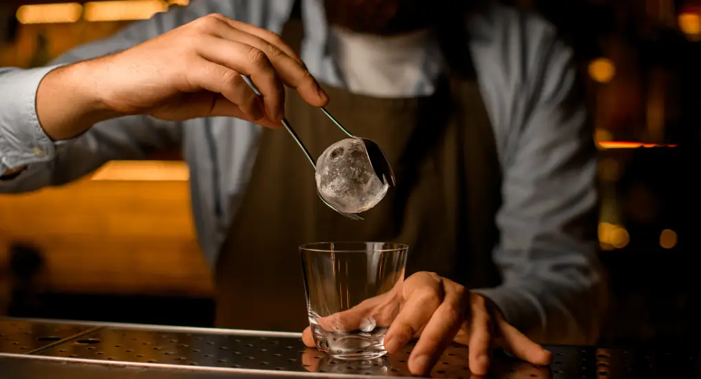 Image of an ice sphere being placed into a whisky/cocktail glass using sustainable ice tools