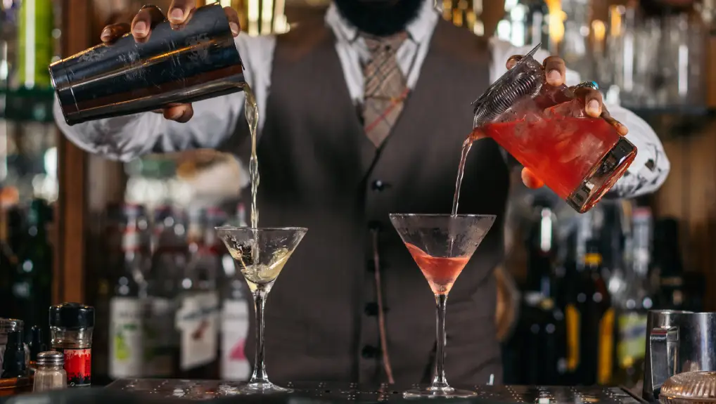 Image of mixologist using shaker and strainer to create cocktails at a bar