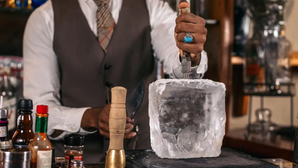 Close-up of an unrecognizable bartender cutting a large ice cube to prepare a cocktail