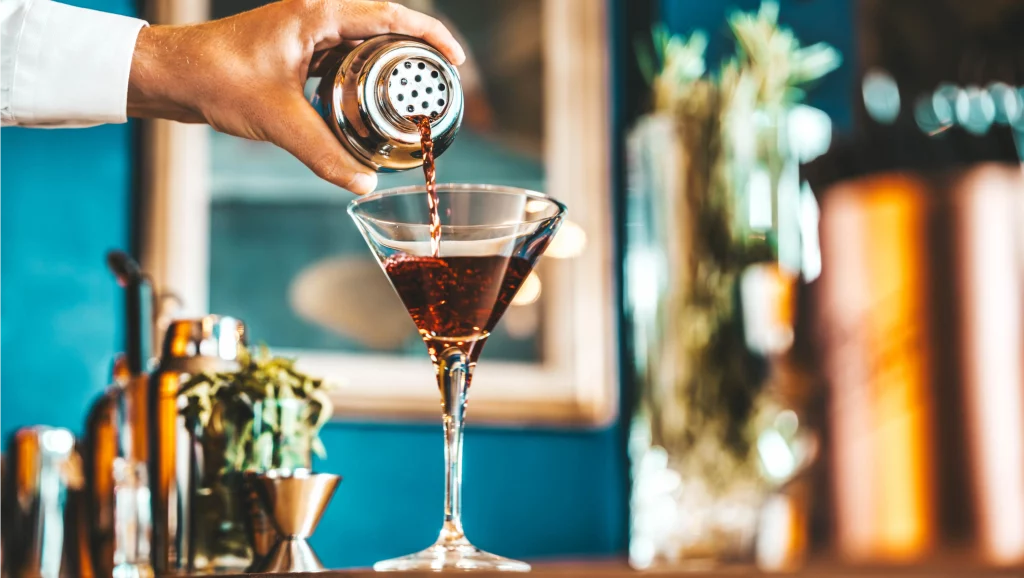 Image of Bartender pouring alcohol from shaker into the glass at cocktail lounge bar venue