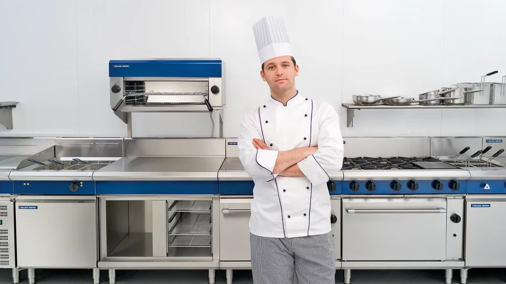 Image of Chef wearing white clothing standing in front of kitchen machinery