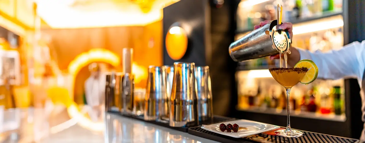 an image of a cocktail being poured though a strainer on a modern ambient-lit bar