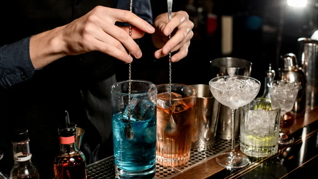 image of cocktail crafting and two brightly coloured drinks being stirred with cocktail spoons