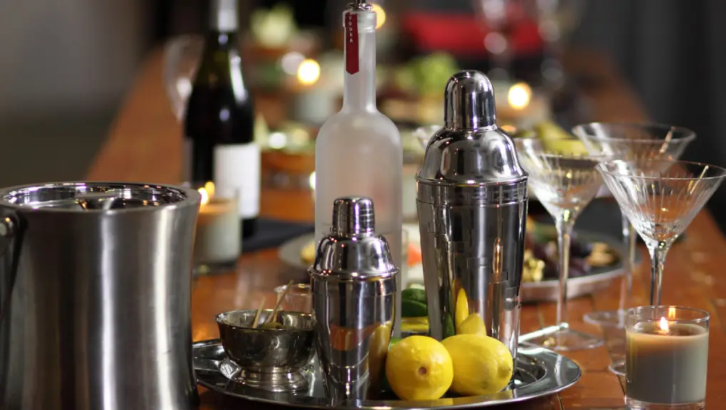 Image of a bar scene with some shakers, shaker accessories and ingredients to make cocktails on a serving tray
