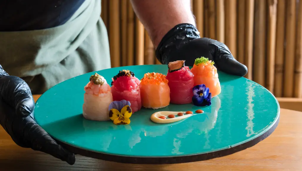 Image of sushi variety adorned with edible flowers presented on a modern plate, embodying cultural restaurant tableware