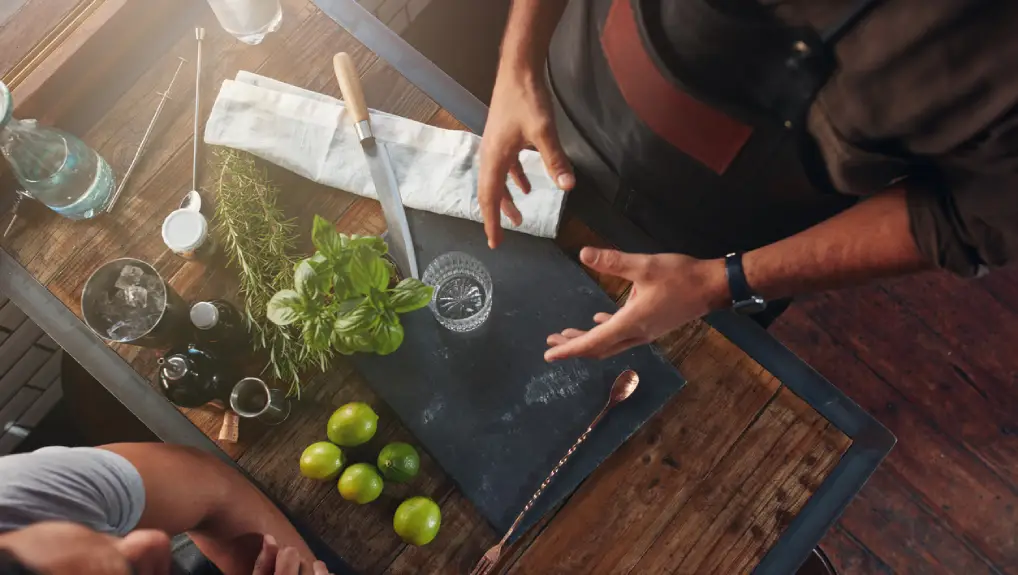 creating new cocktail recipe and taking down notes. Top view of man pouring mixture into a jigger to prepare a cocktail and another taking down notes.