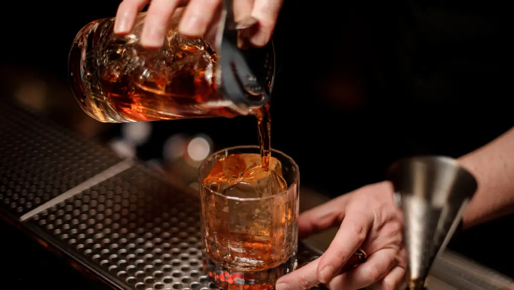 image of a male bartender pouring alcohol cocktail using glass with steel strainer