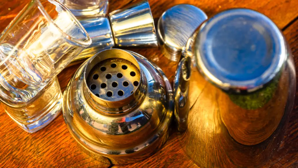 Image of cocktail shaker and accessories with shot glasses on a wooden board. Bar utensils