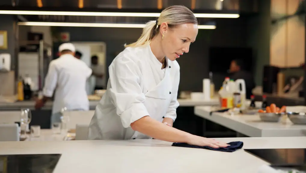 Image of woman, cleaning and chef wipe counter for dinner rush prep, hygiene and bacteria removal- catering equipment maintenance
