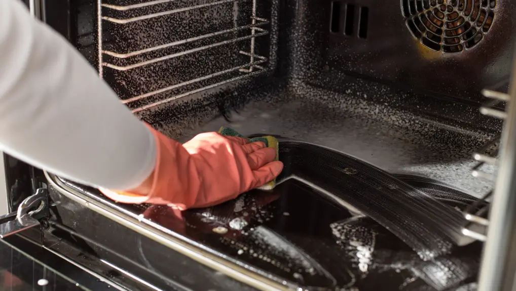  hands with protective gloves scrubbing oven in kitchen