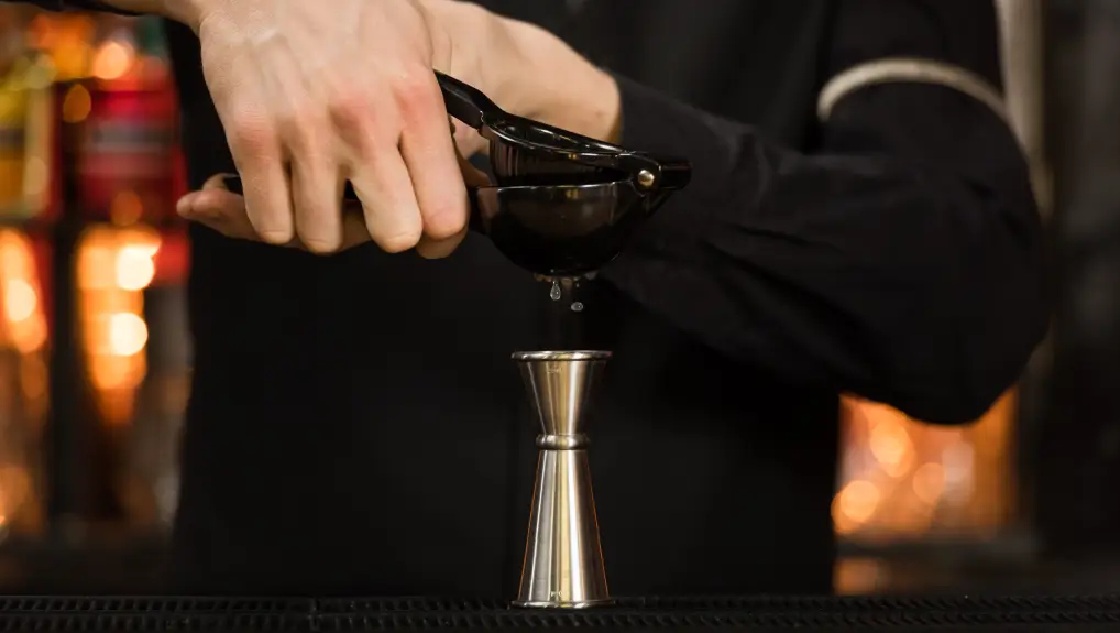 Image of mexican elbow being used with a jigger in an ambient lit bar - by Beaumont