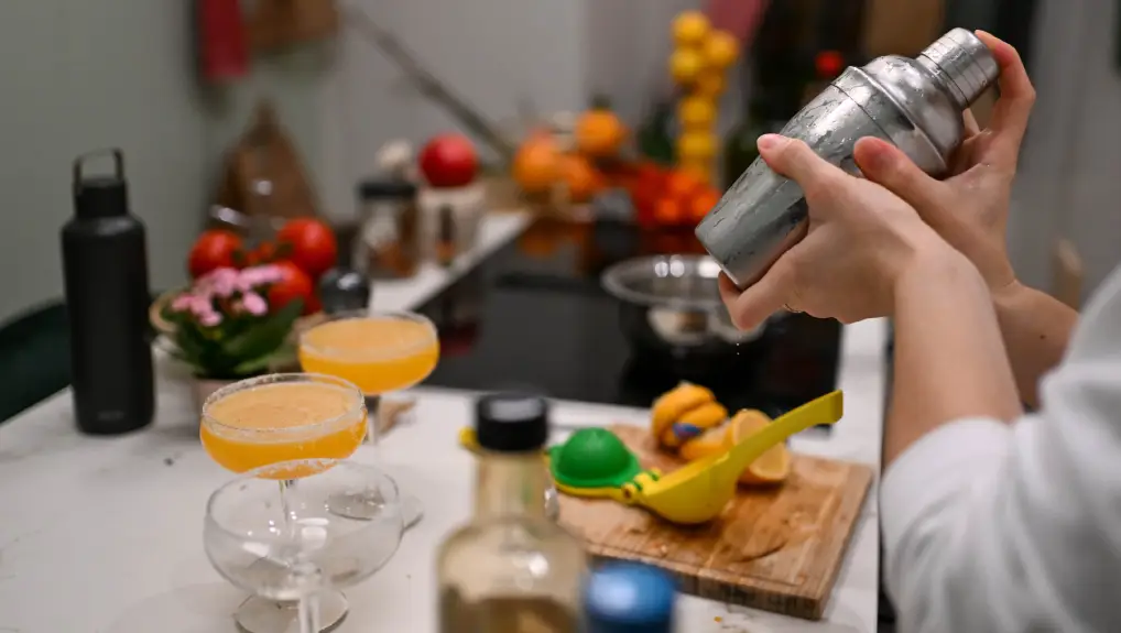 Image of A person is shaking a stainless steel cocktail shaker over a white countertop. bar accessories budget vs premium